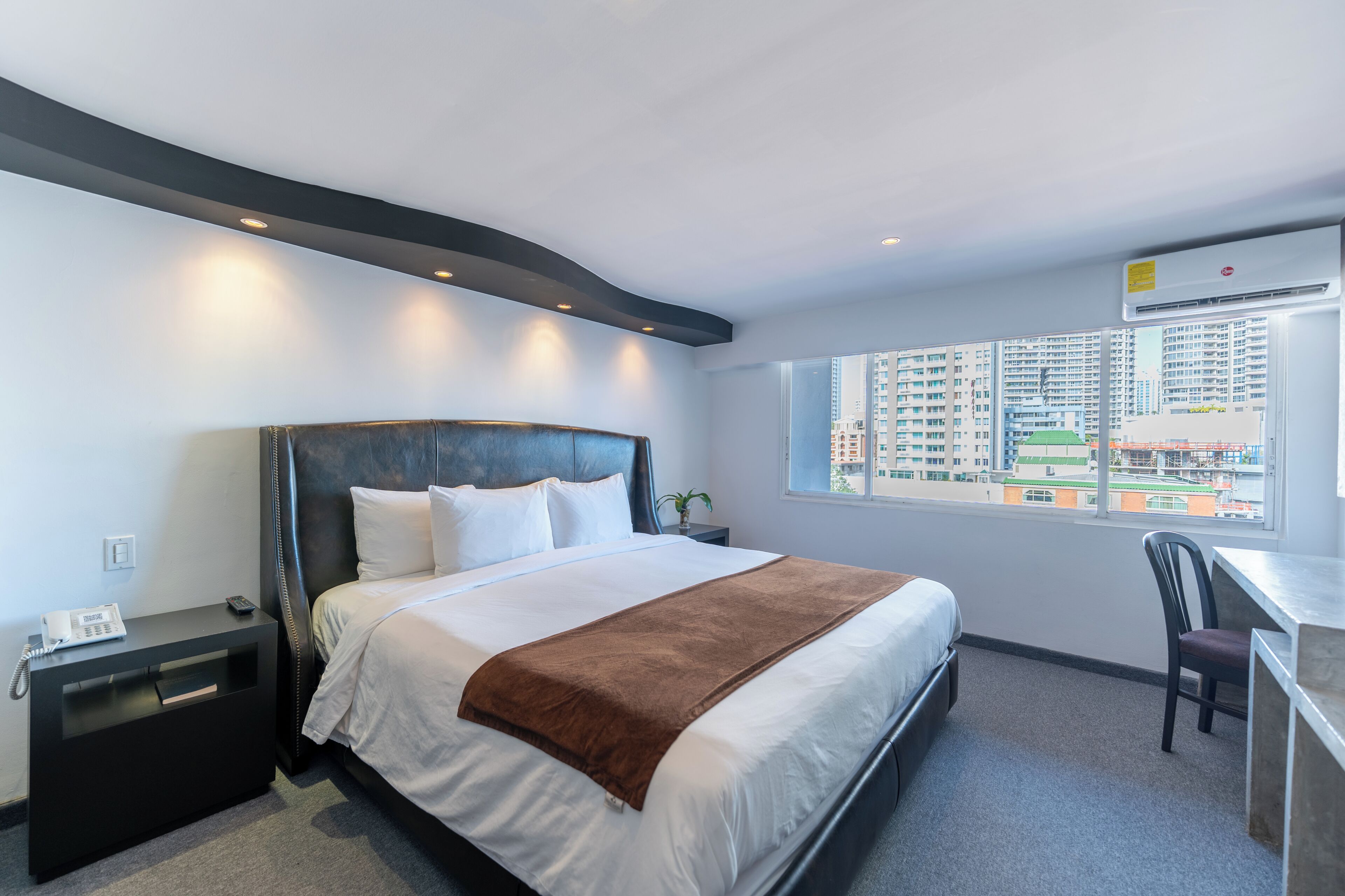 Habitación de hotel con cama, mesita de noche y ventana con vista a la ciudad.