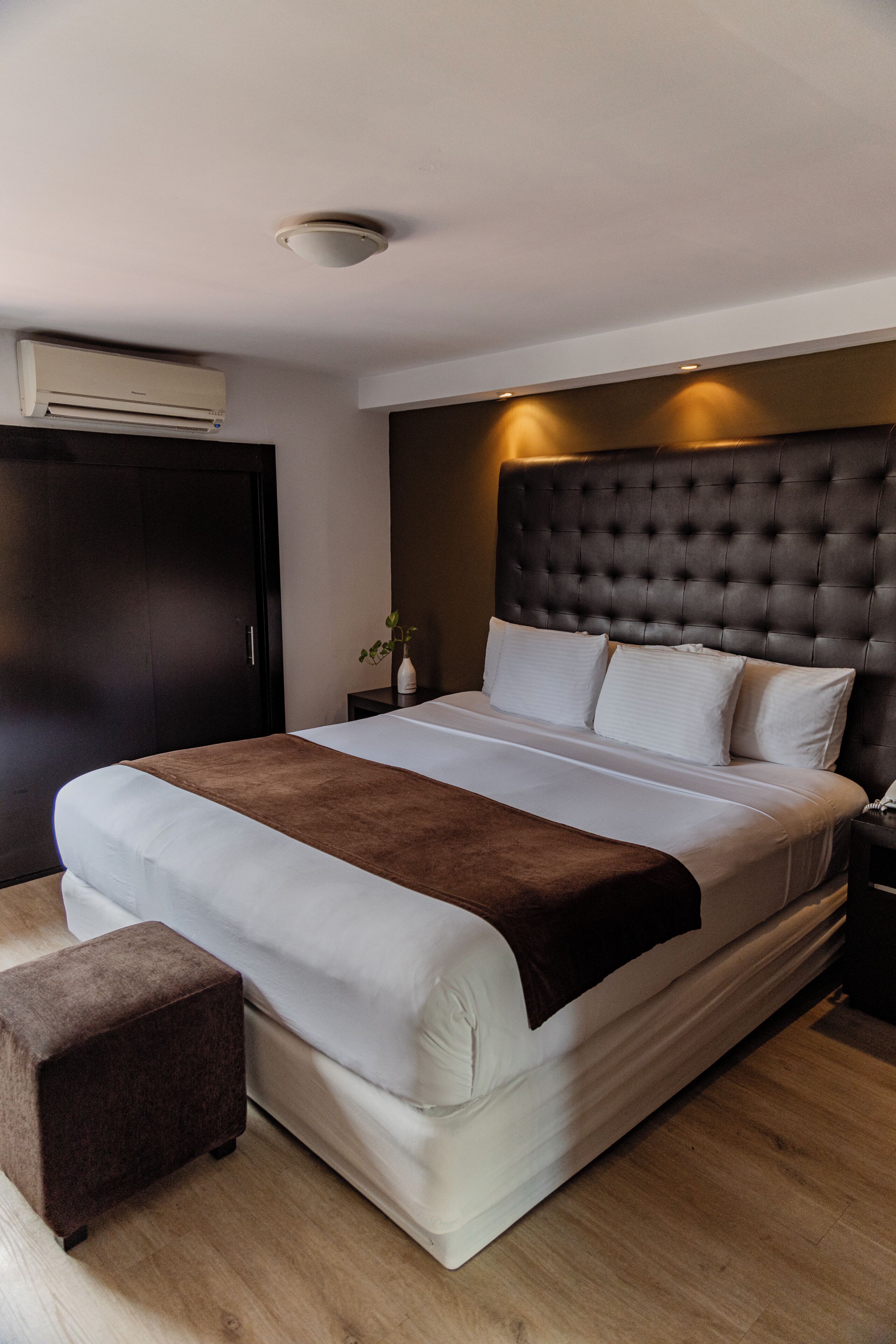 Une chambre d’hôtel avec un grand lit, une table de chevet, une commode, une armoire et un luminaire au plafond.