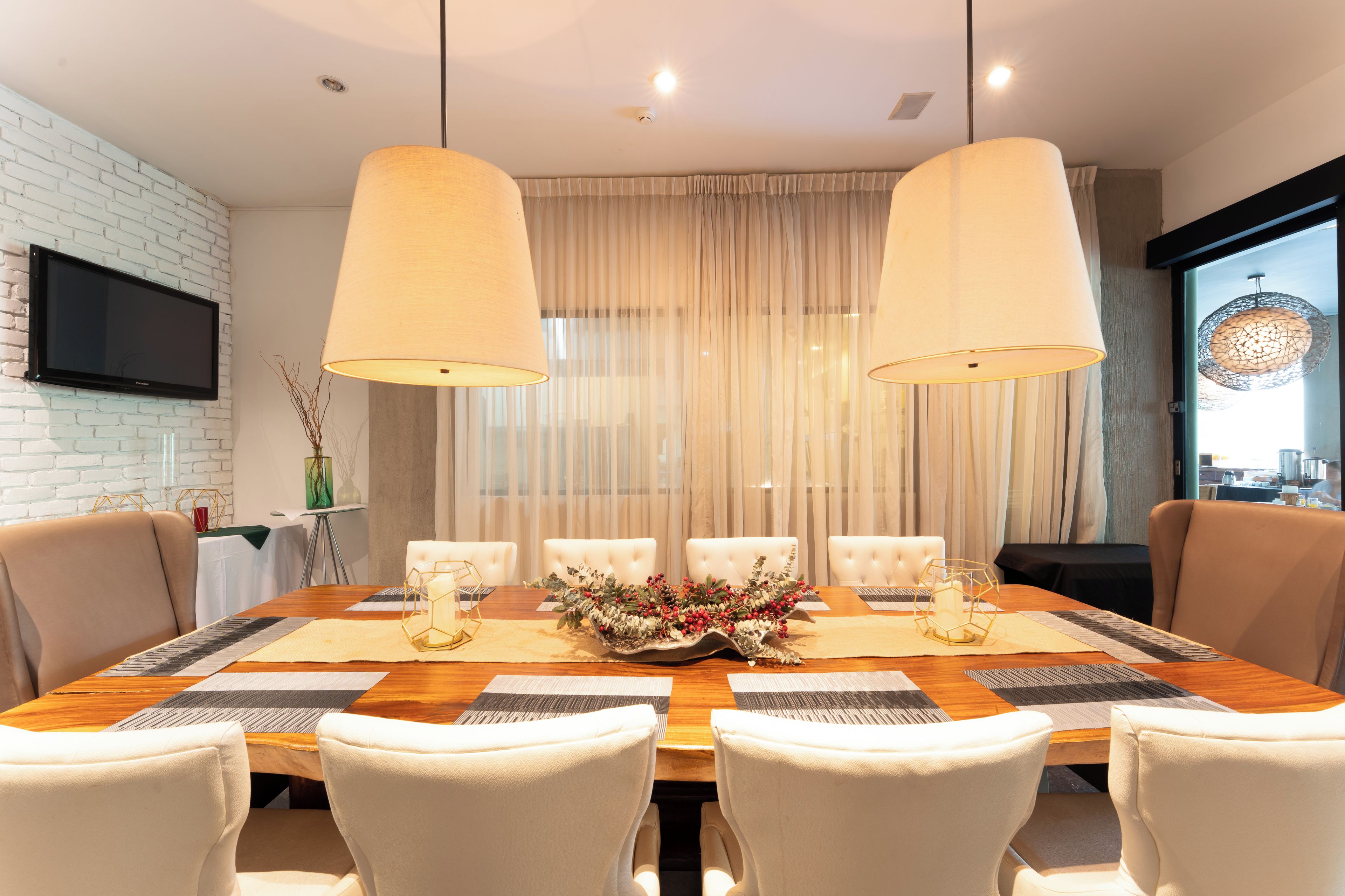 Comedor con mesa de madera, sillas blancas y dos lámparas colgantes.