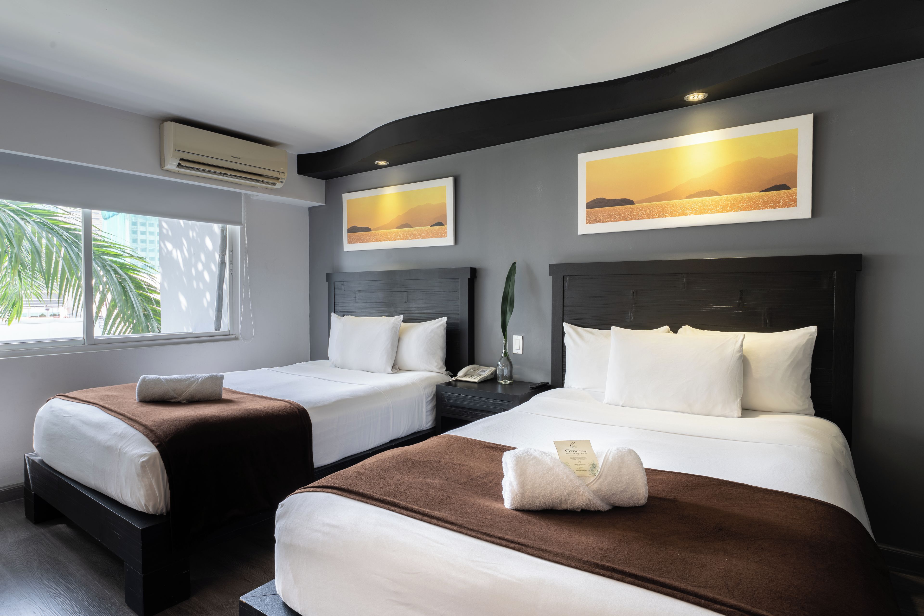 Une chambre d’hôtel avec deux lits, une fenêtre donnant sur un beau paysage et des œuvres d’art accrochées aux murs.