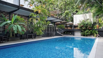 A swimming pool with a tiled edge, surrounded by lush greenery and outdoor seating.