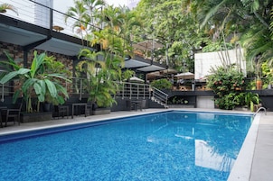 Una piscina con borde de azulejos, rodeada de exuberante vegetación y mobiliario exterior.