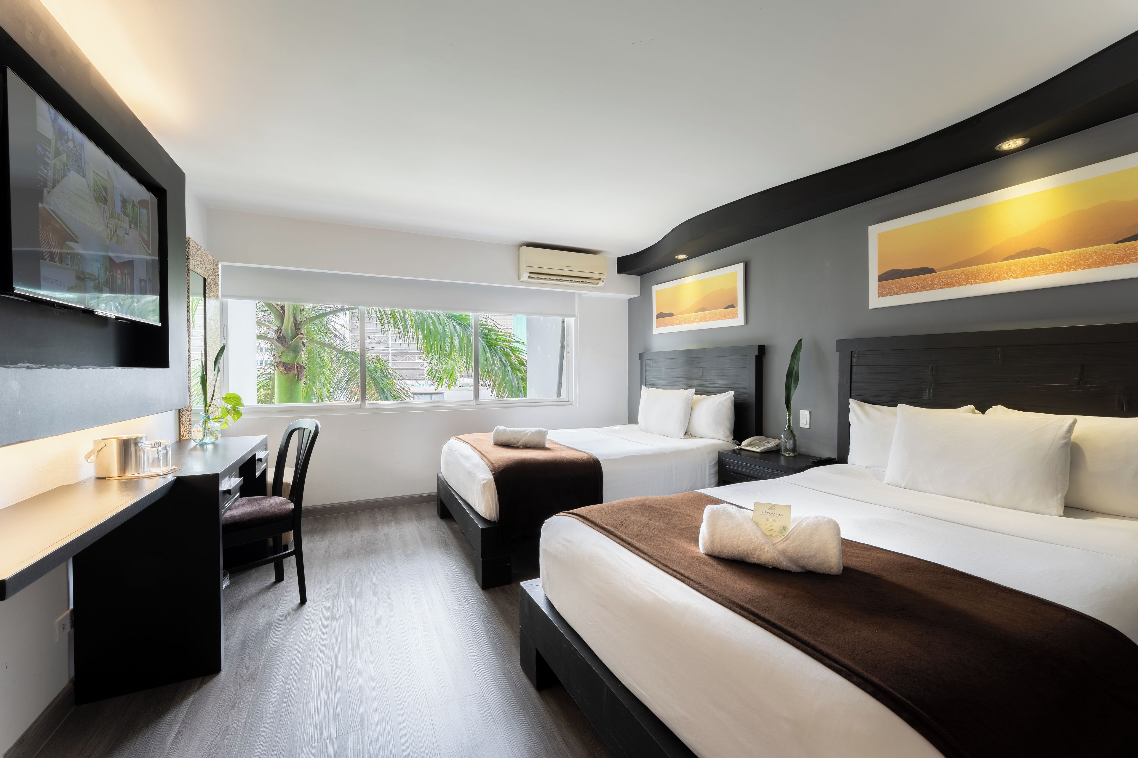 Una habitación de hotel con cama, mesita de noche, silla, escritorio y un ventanal grande.