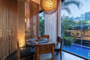A dining area with a round table, chairs, and a view of a swimming pool and palm trees.
