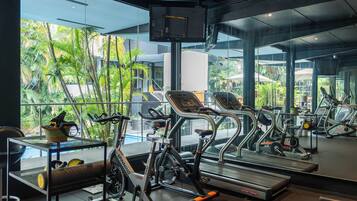 Un gimnasio con equipo de ejercicio, cinta de correr y un espejo que refleja el interior.
