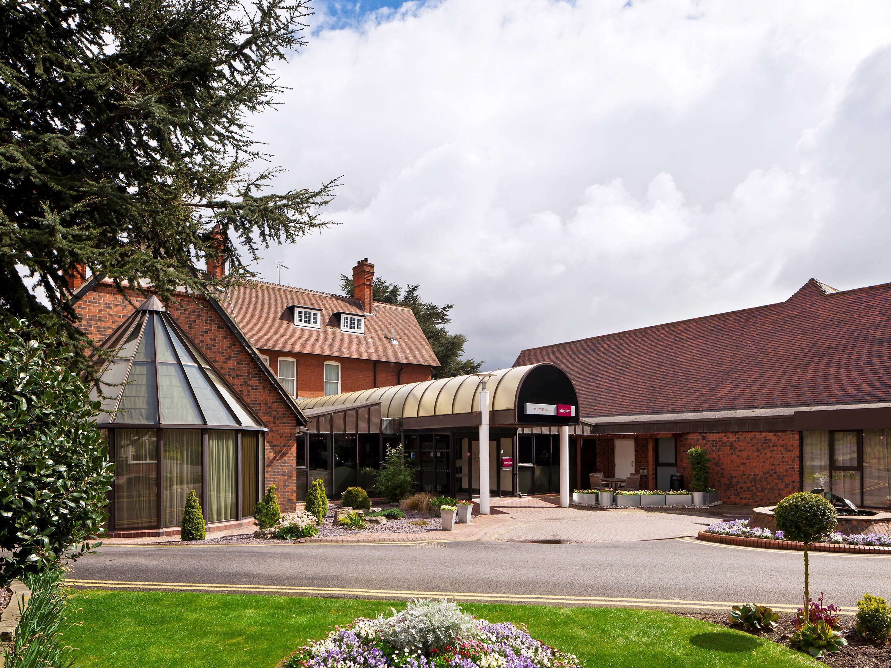 A hotel with a glass conservatory, a covered entrance, and a brick building with a red-tiled roof.