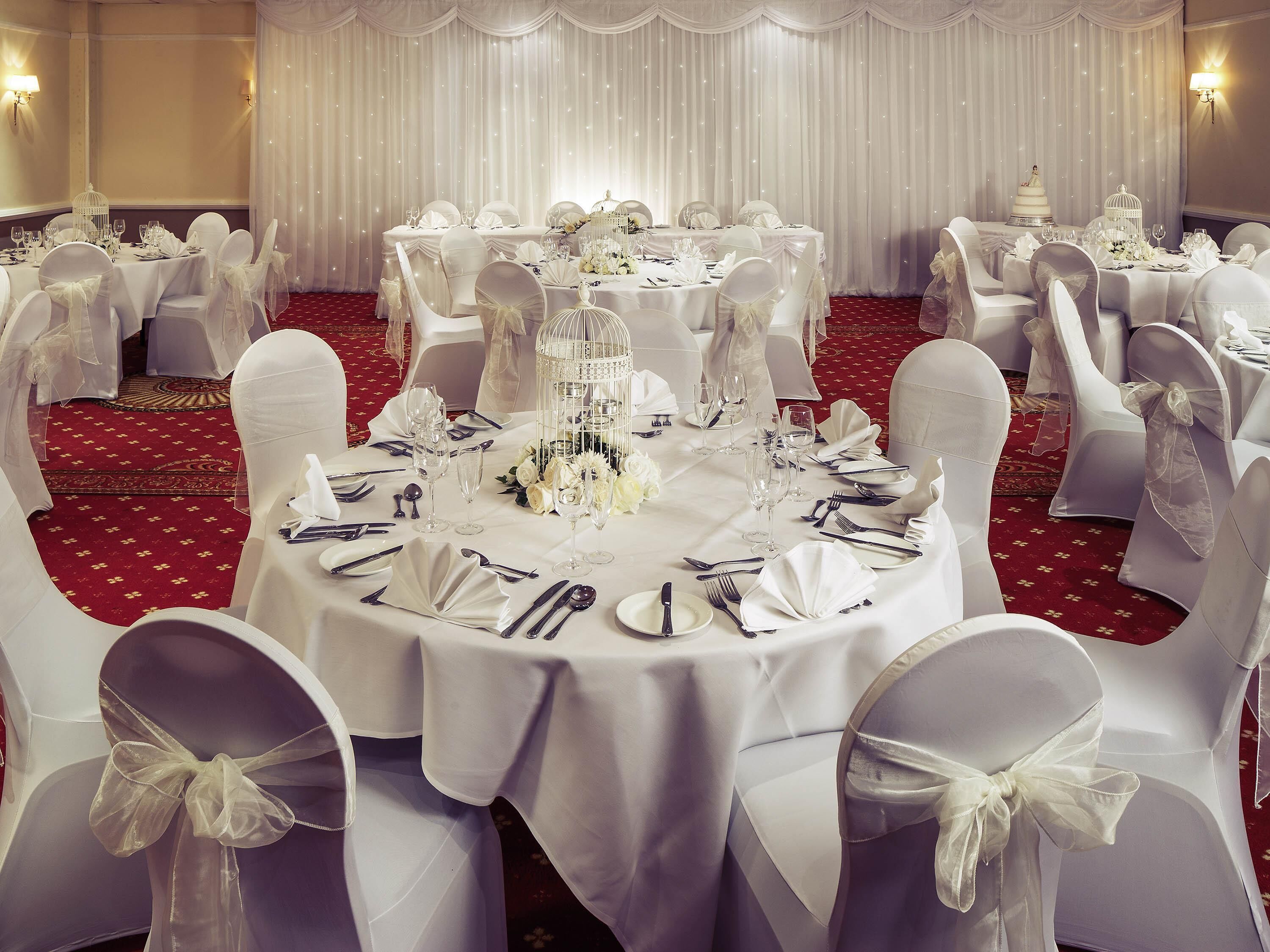 A banquet hall with round tables, white tablecloths, and chairs with white sashes.