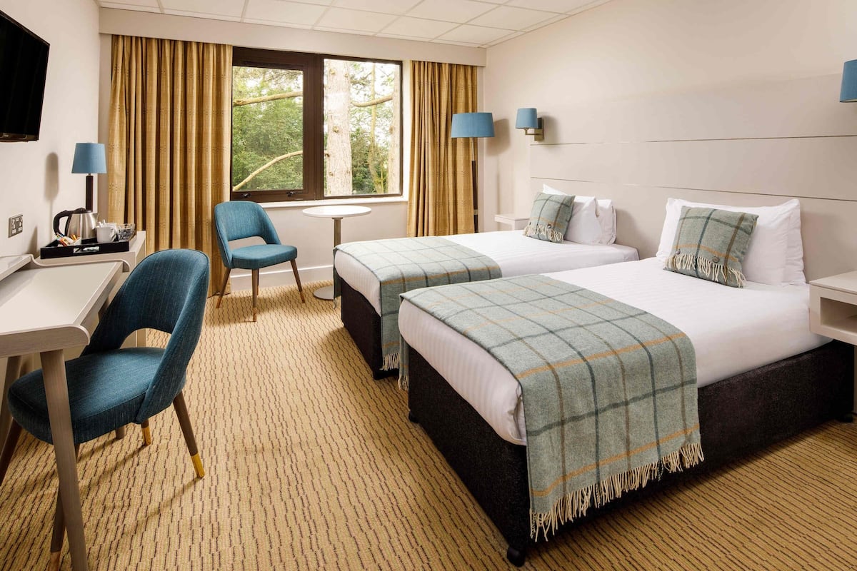 Une chambre d’hôtel avec deux lits, un bureau, une chaise, une petite table et une fenêtre avec des rideaux.