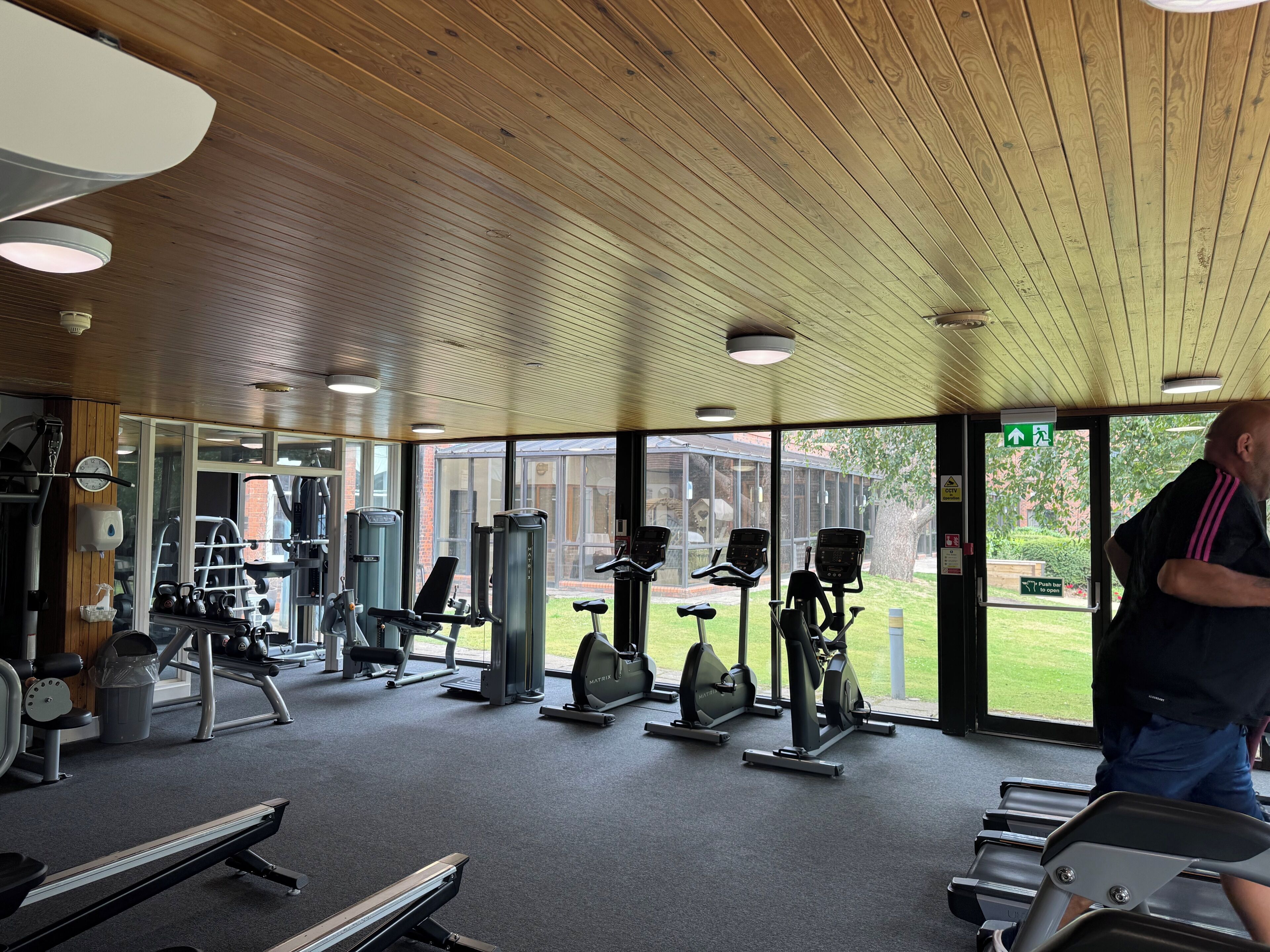 A gym with various exercise equipment, large windows, and a wooden ceiling.