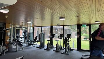 Un gimnasio con diversos equipos de ejercicio, amplias ventanas y techo de madera.