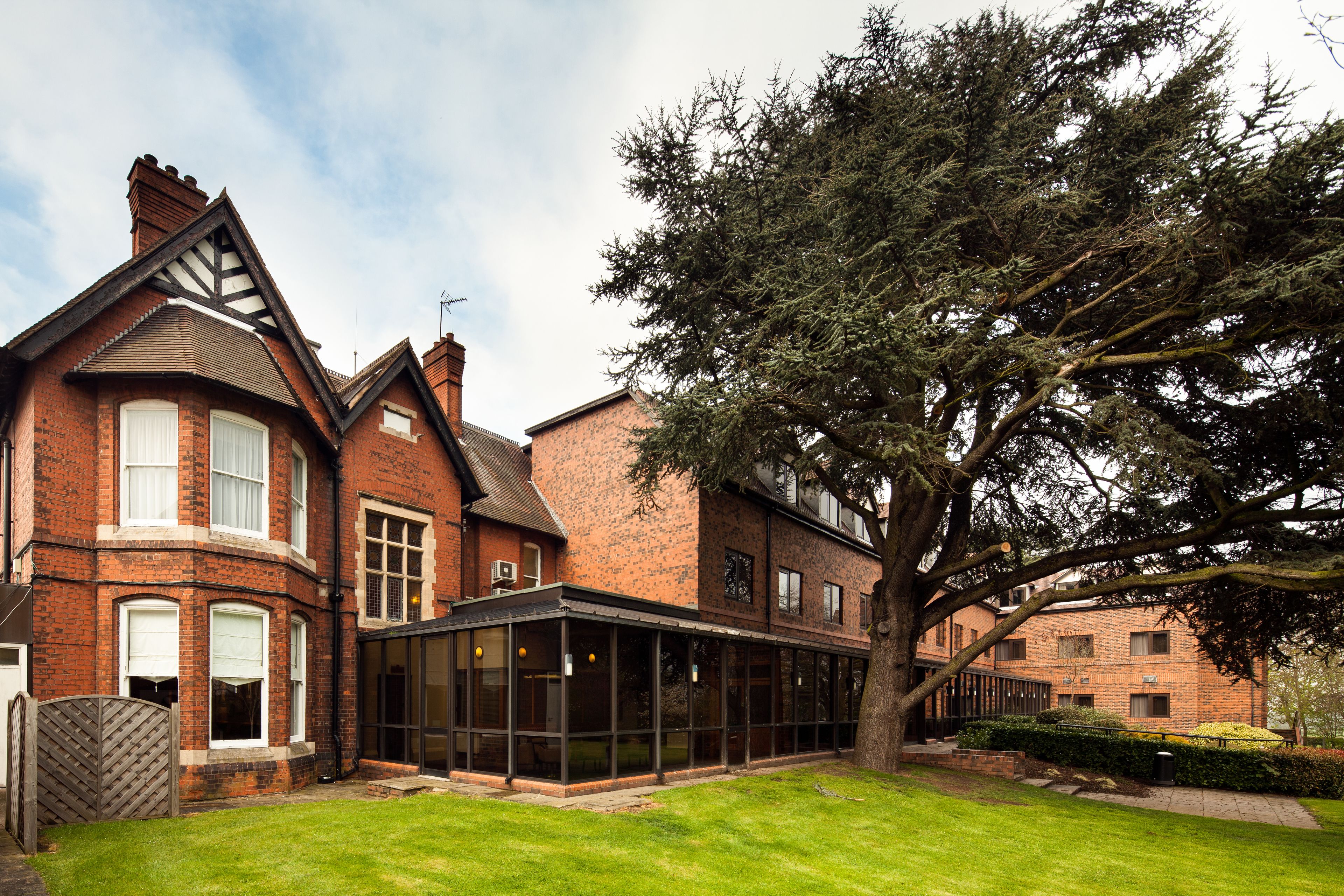 A large brick house with a conservatory, a large tree, and a well-maintained lawn.