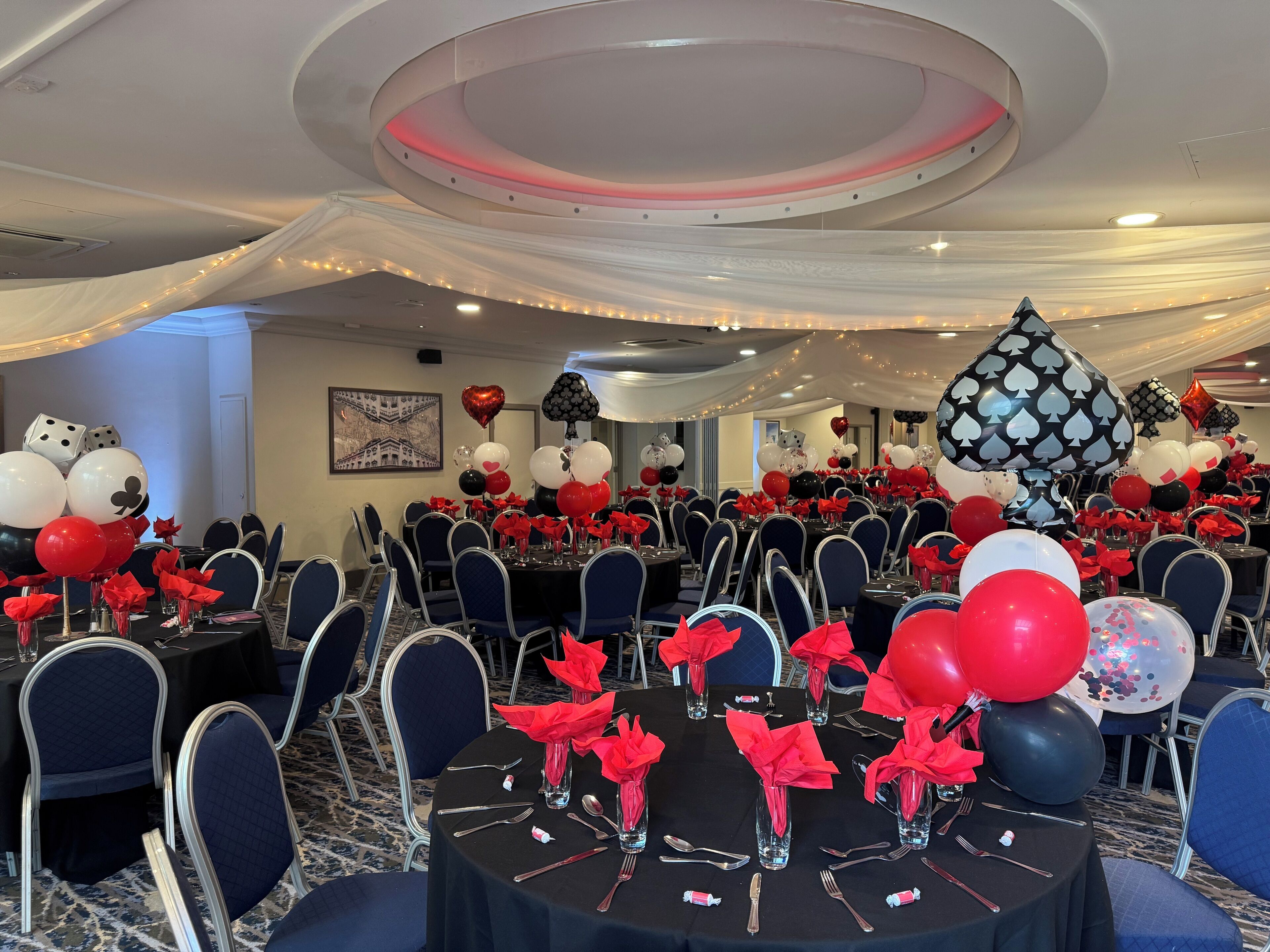 A banquet hall with round tables, chairs, and red napkins.