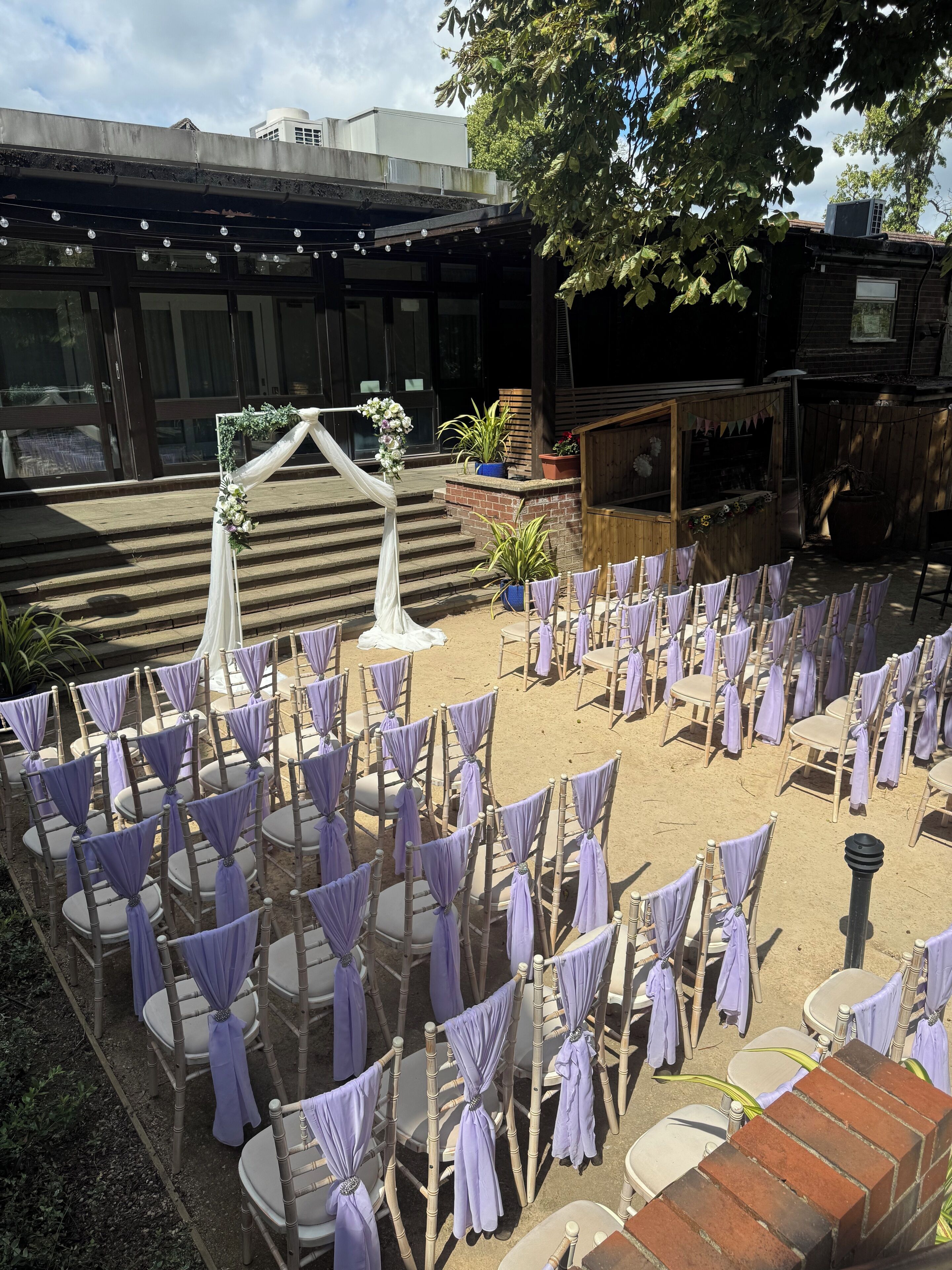 An outdoor seating area with rows of chairs and a stage with floral decorations.