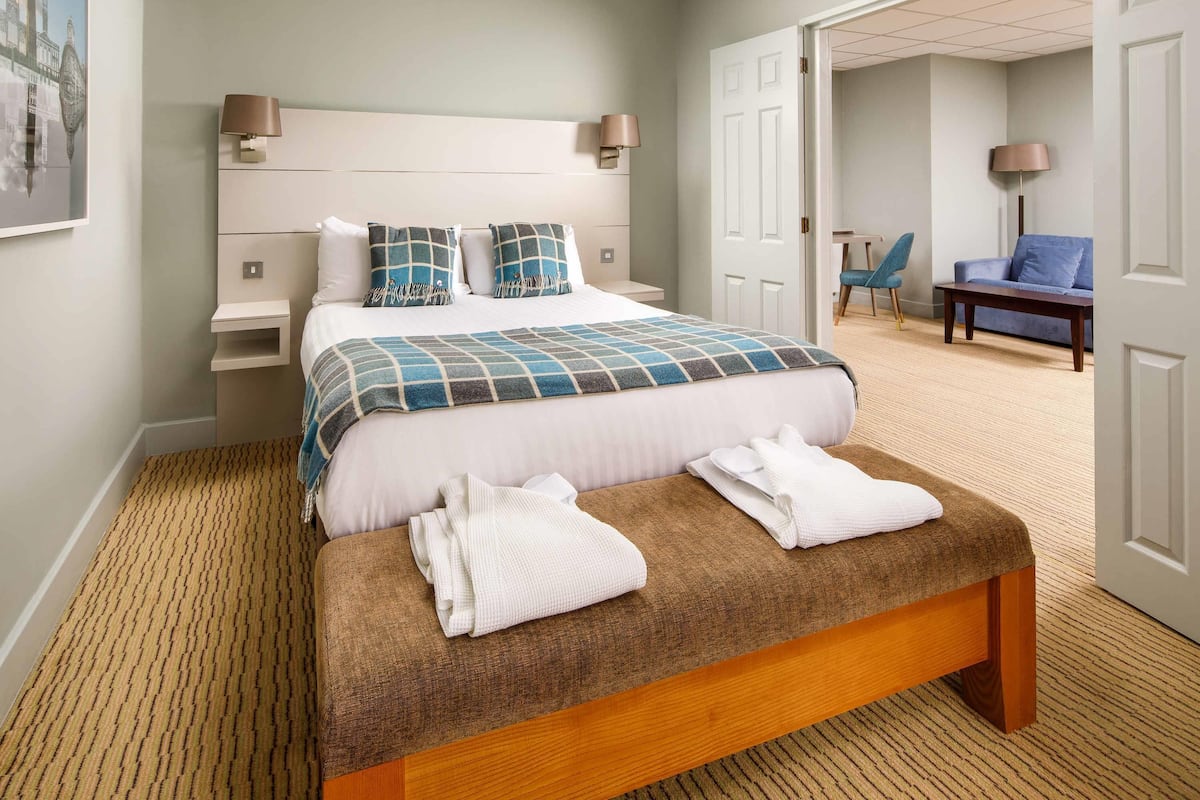 Une chambre d’hôtel bien rangée, avec un lit, des tables de chevet, un banc et une chaise.