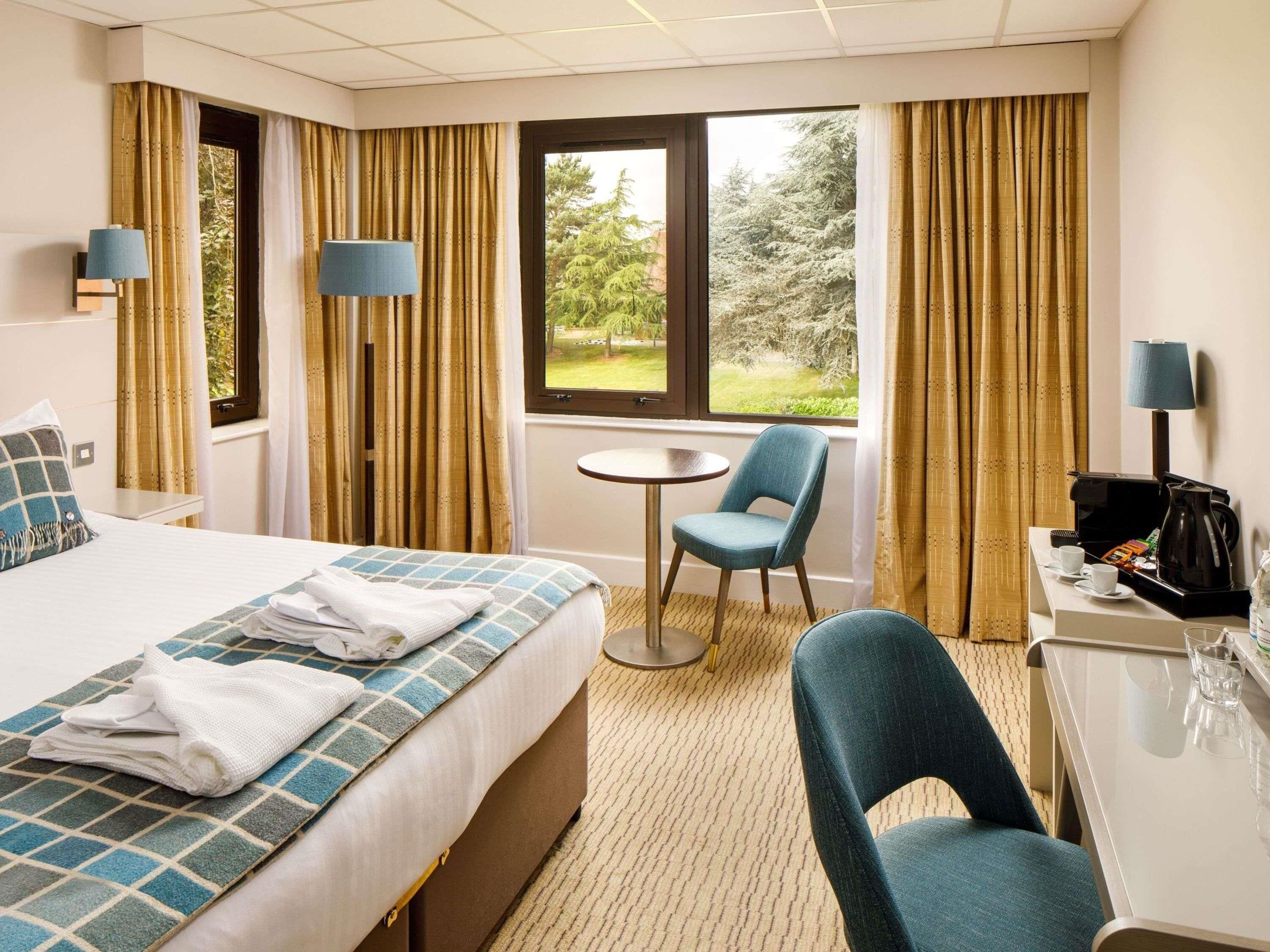 A hotel room with a bed, a desk, a chair, a coffee maker, and a window with a view of trees.