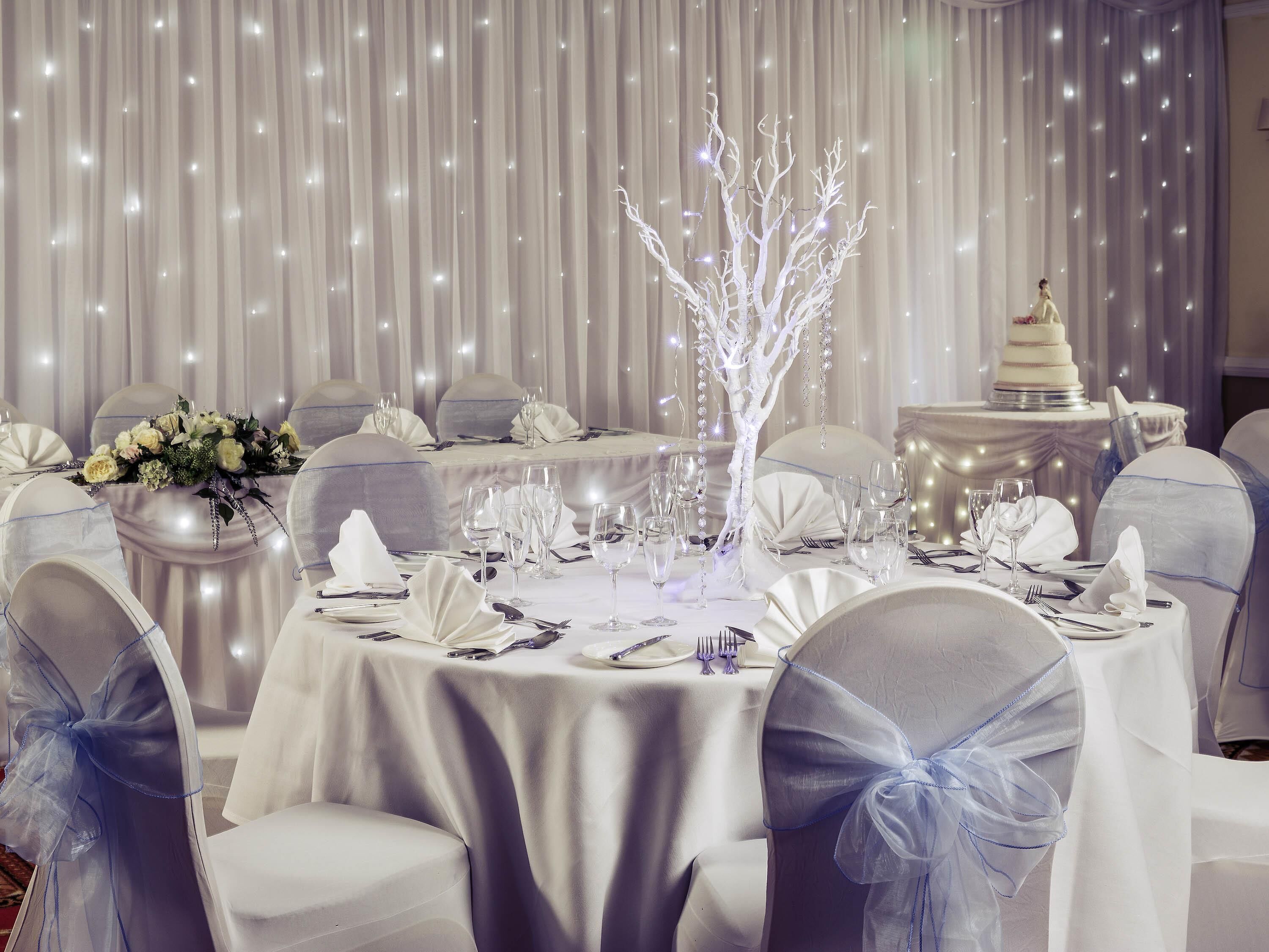 A banquet hall with round tables, white tablecloths, and chairs with blue sashes.