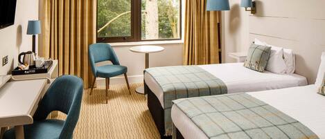 A hotel room with a desk, two beds, a chair, a small table, and a TV.