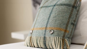 A plaid pillow with buttons and fringe on a bed.