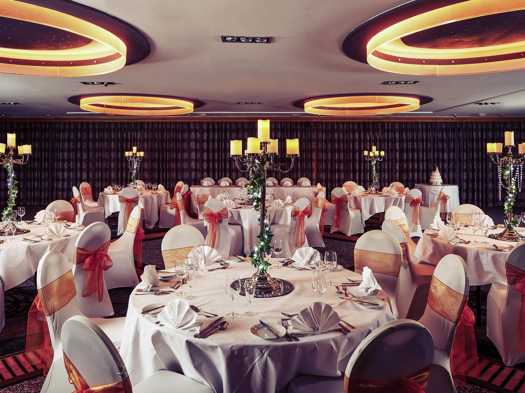 A banquet hall with round tables, white tablecloths, and chairs with red sashes.