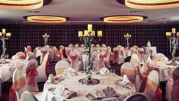 A banquet hall with round tables, white tablecloths, and chairs with red sashes.