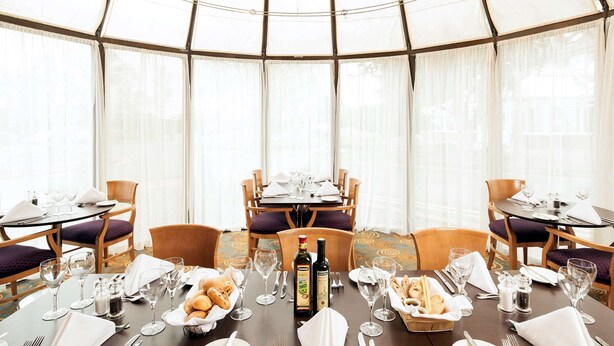 Comedor con mesas dispuestas para cuatro, cada una con sillas, platos, cubiertos, vasos y una botella de aceite de oliva.