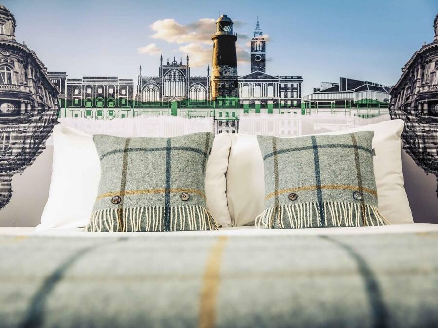 Una cama con dos almohadas frente a un fondo de paisaje urbano con edificios históricos y una torre del reloj.