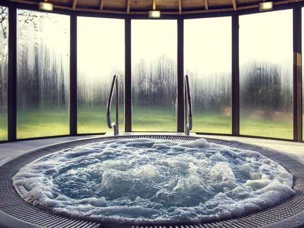 A hot tub with a view of a snowy landscape through large windows.