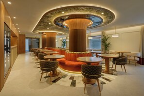 Un interior moderno con una zona de estar central, varias mesas y un diseño de techo único.