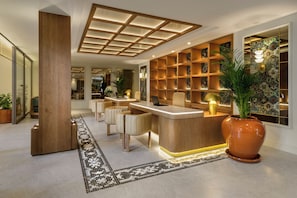 A modern reception area with a wooden reception desk, seating, and a patterned wall. - Palacio San Juan, A Royal Hideaway Hotel (Murcia)