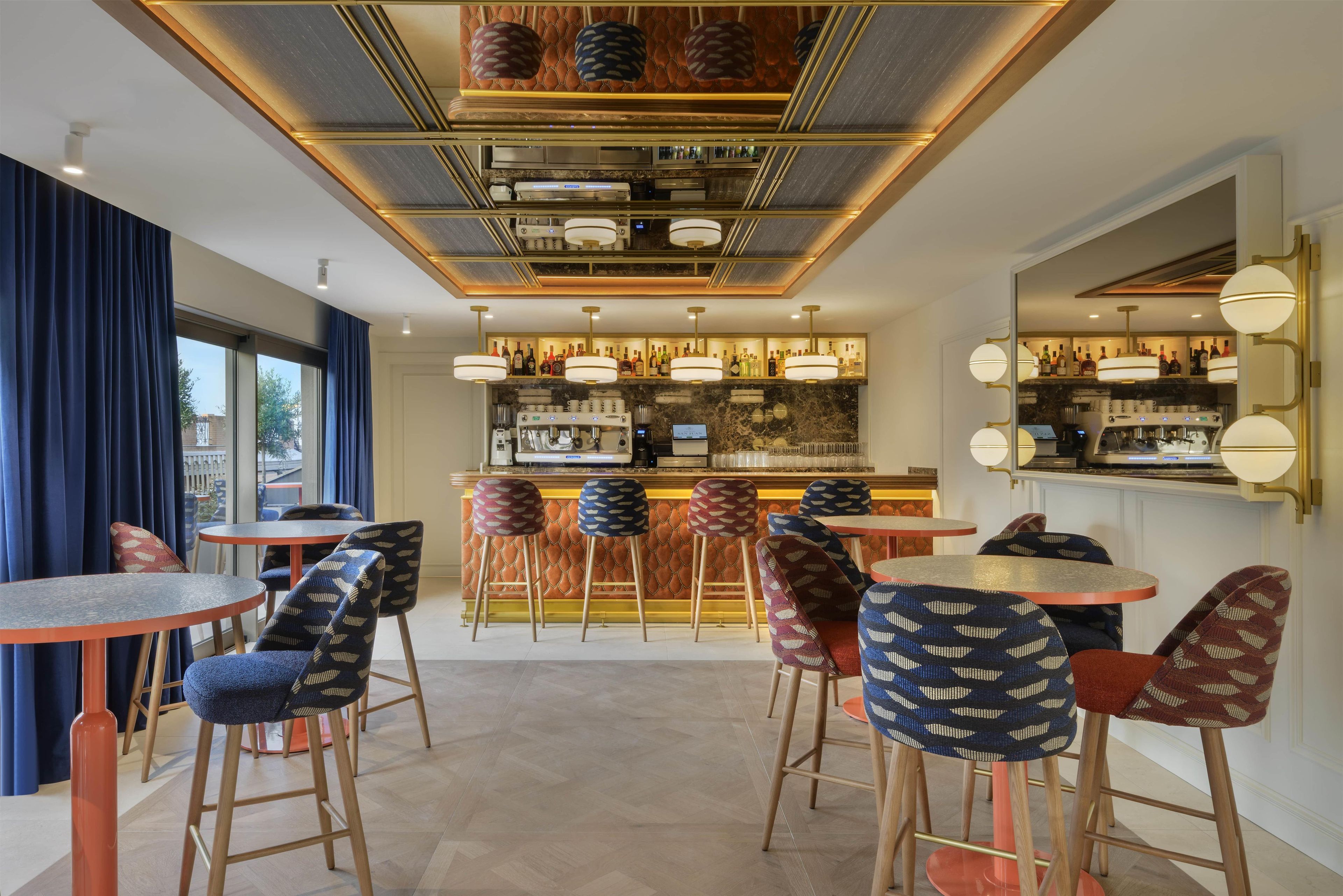 Zona de bar con varios taburetes y mesas, barra con diferentes botellas e iluminación decorativa en el techo.