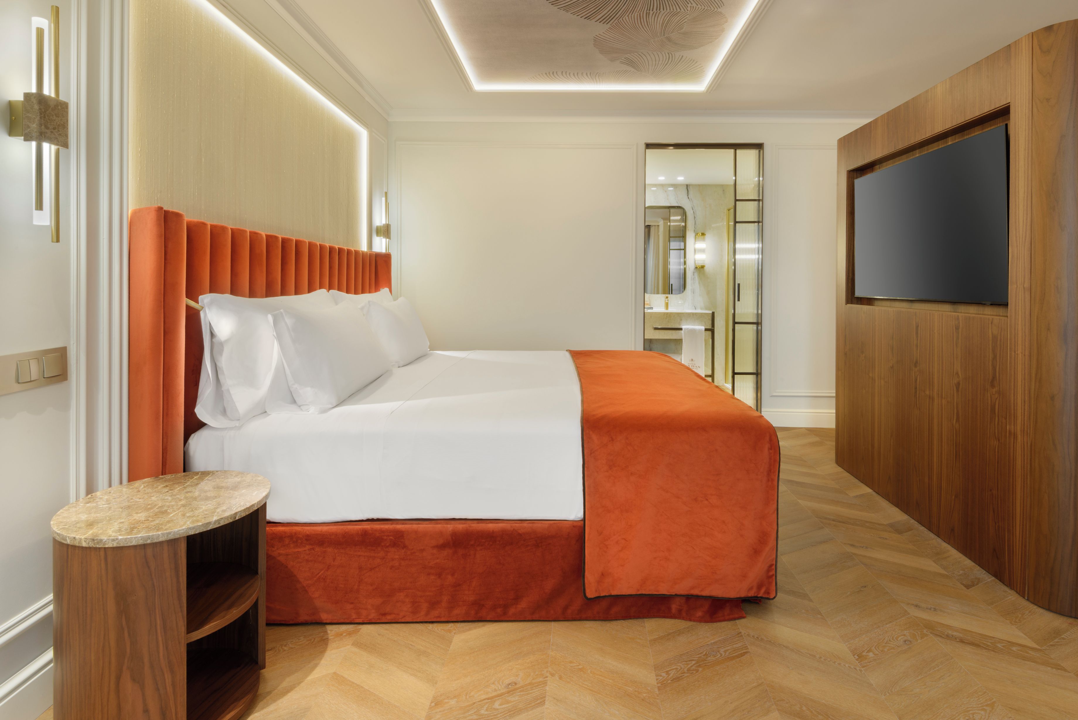 A hotel room with a bed, a TV, a wooden wardrobe, and a bathroom visible through an open door.