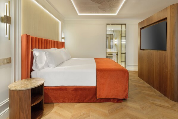Habitación de hotel con cama, televisión, armario de madera y baño visible a través de una puerta abierta.