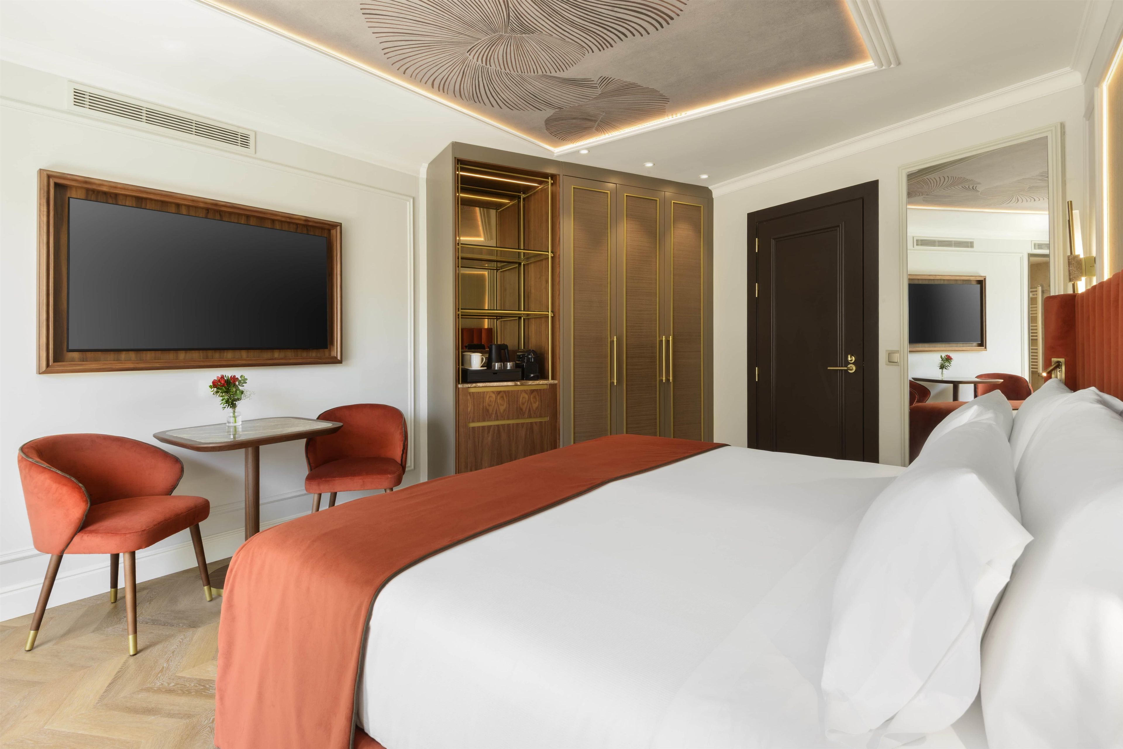 A hotel room with a large bed, a desk with a chair, a wardrobe, and a television on the wall.