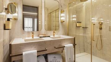 Un baño moderno con tocador de mármol, doble lavamanos, un espejo grande y zona de ducha con mampara de vidrio.