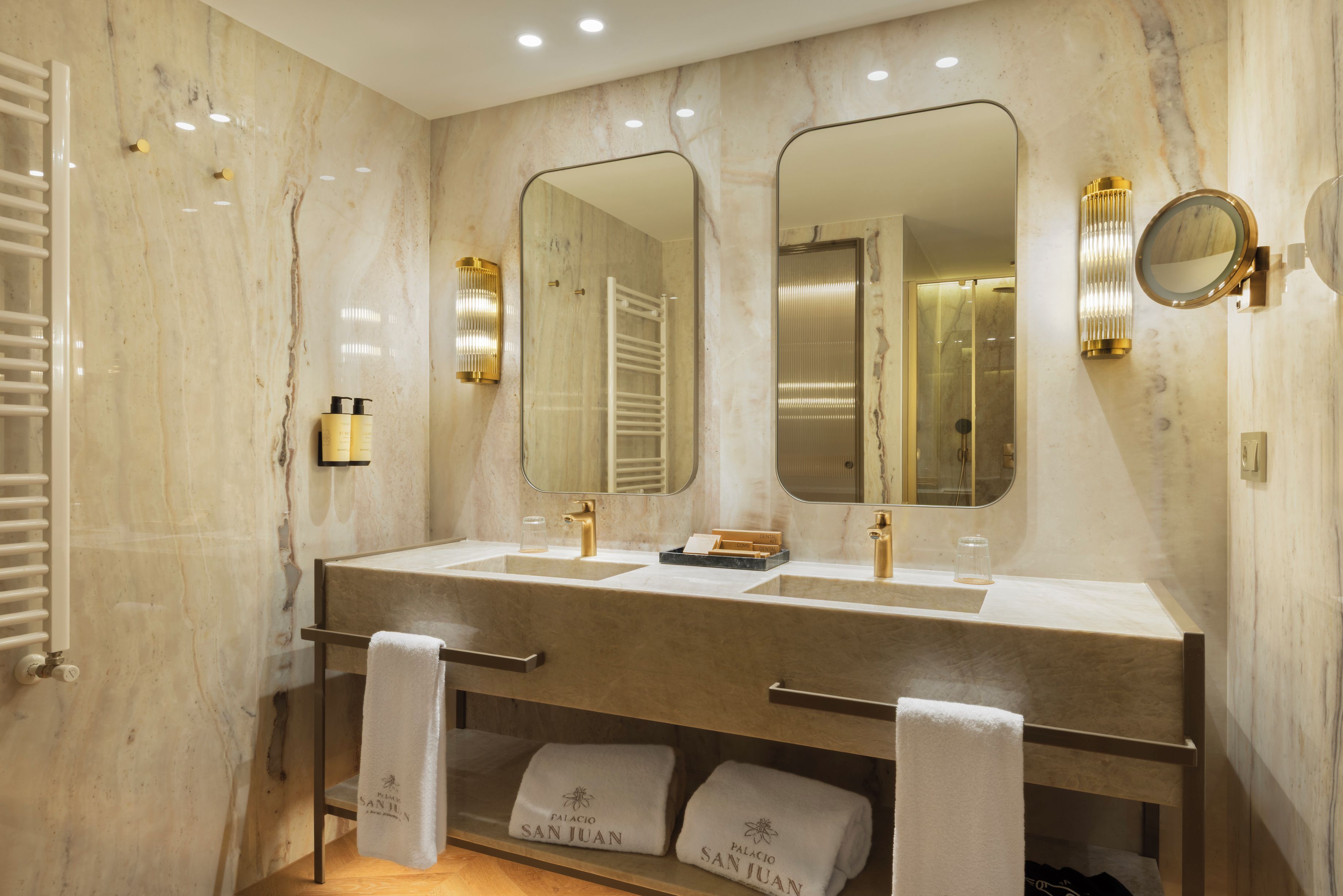 Un baño moderno con paredes de mármol, lavamanos dobles y un espejo grande.