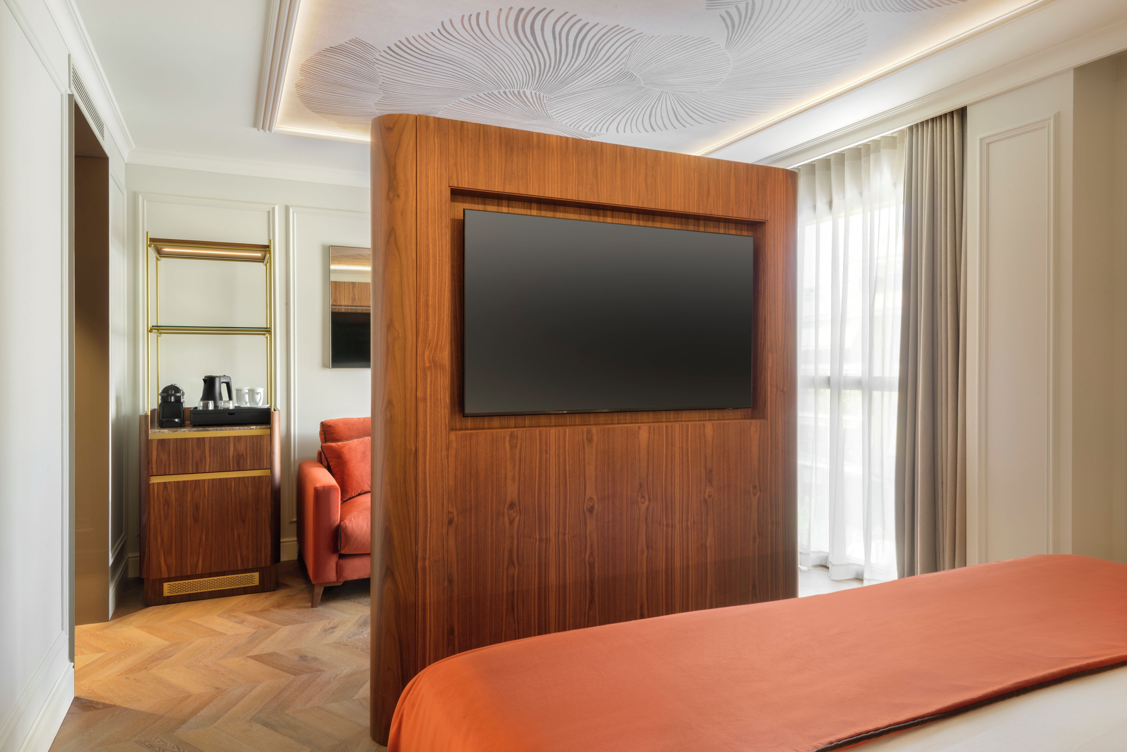 Habitación de hotel con una cama grande, pared revestida de madera, televisor de pantalla plana, cómoda de madera, una silla roja y un espejo grande.