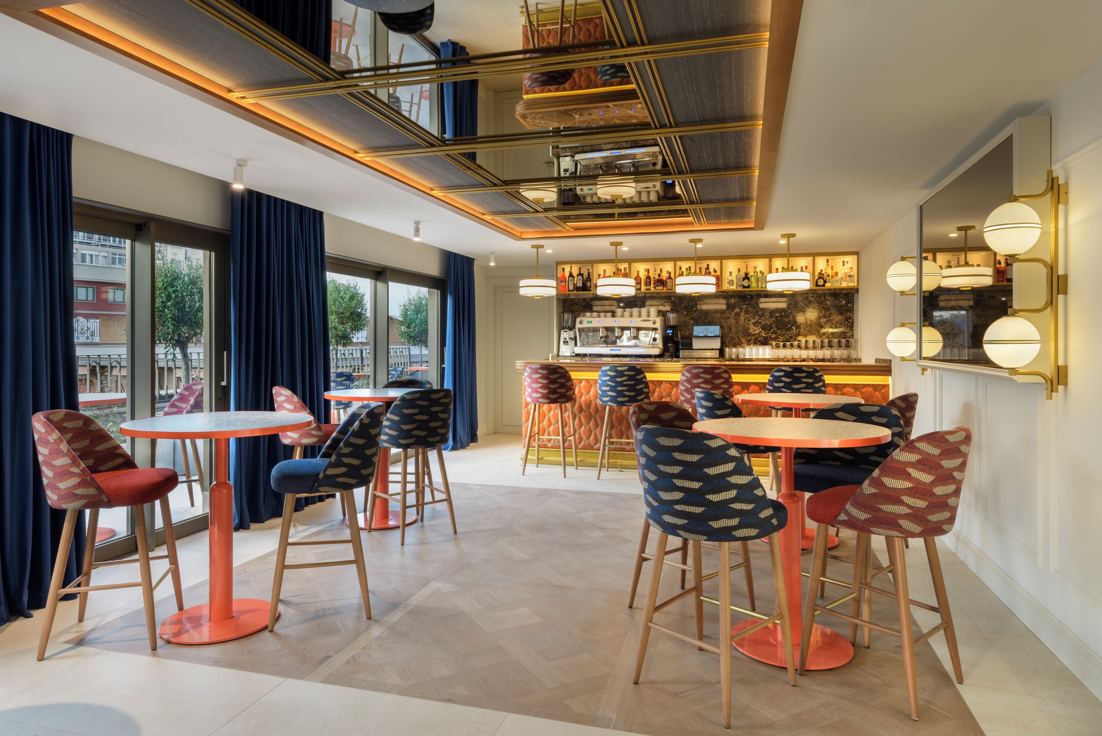 A modern bar area with multiple seating options, including round tables and bar stools, and a bar counter with a variety of bottles.