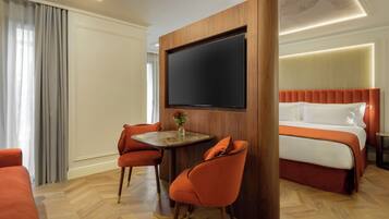 Een hotelkamer met een bed, een televisie, twee stoelen, een klein tafeltje en een raam met gordijnen.