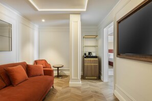 Habitación de hotel con sofá, una pequeña mesa redonda, minibar y un espejo grande.