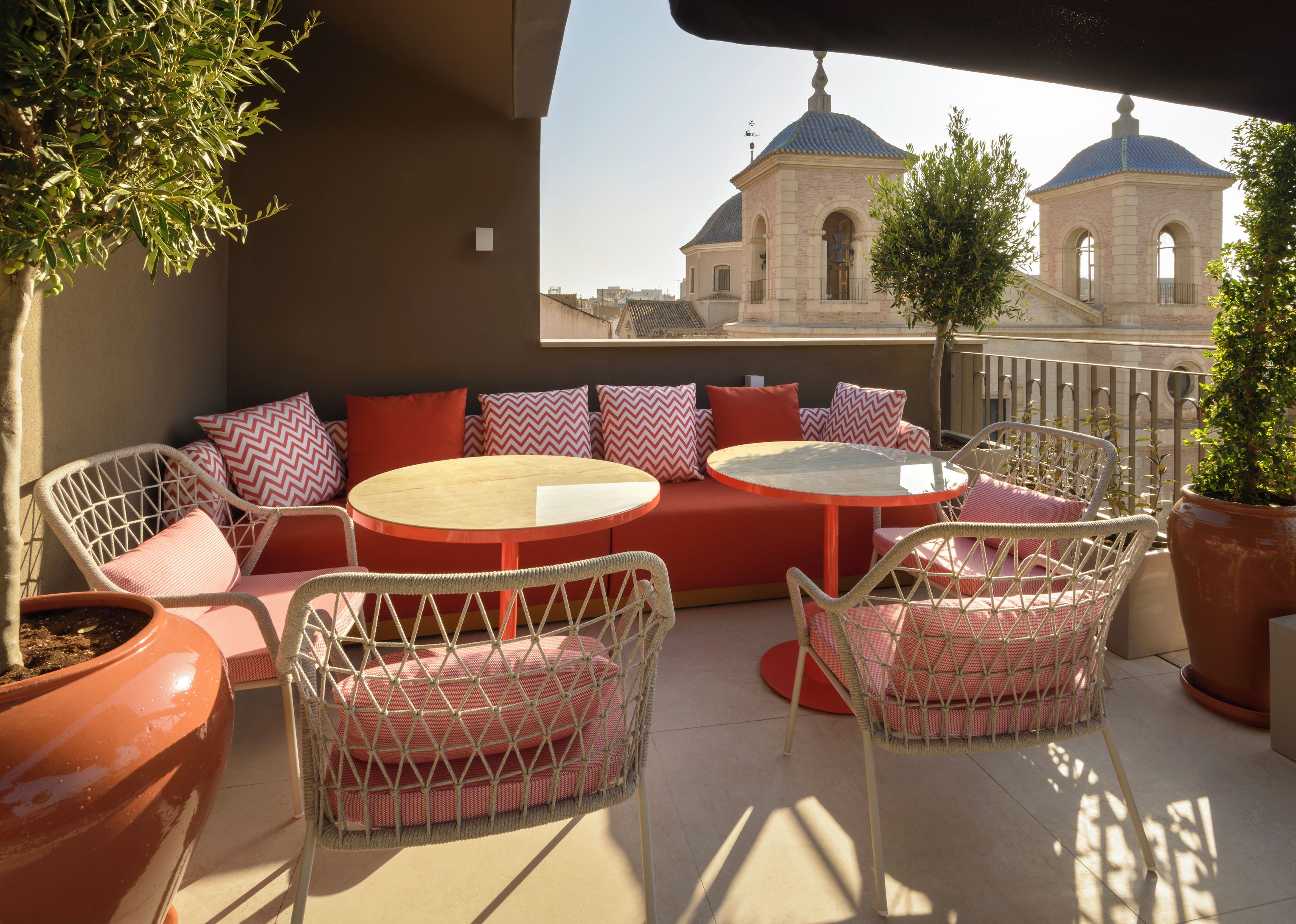 Un área de estar al aire libre con sillas de mimbre y una mesa redonda, con vista a un edificio con techos abovedados.