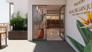 A modern hotel entrance with a glass door, a bar area visible through the door, and a sign reading "Palacio Real de San Juan". - Palacio San Juan, A Royal Hideaway Hotel (Murcia)