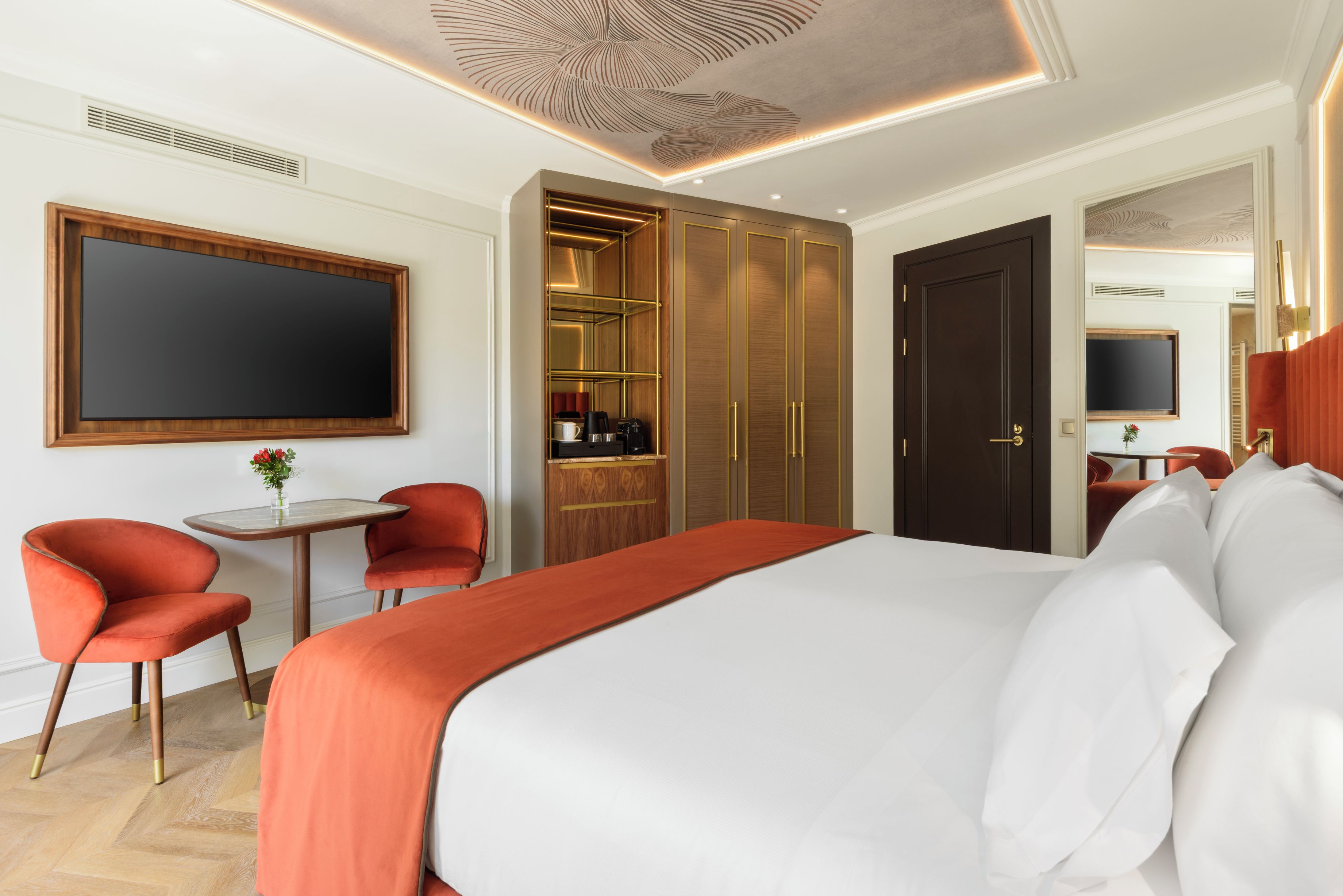A hotel room with a large bed, a desk with a chair, a wardrobe, and a television mounted on the wall.