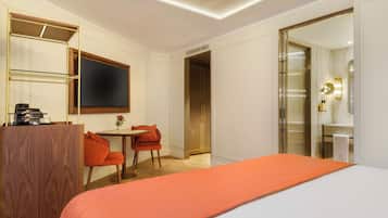 Habitación de hotel con cama, escritorio con silla, televisión y baño con espejo y lavamanos.