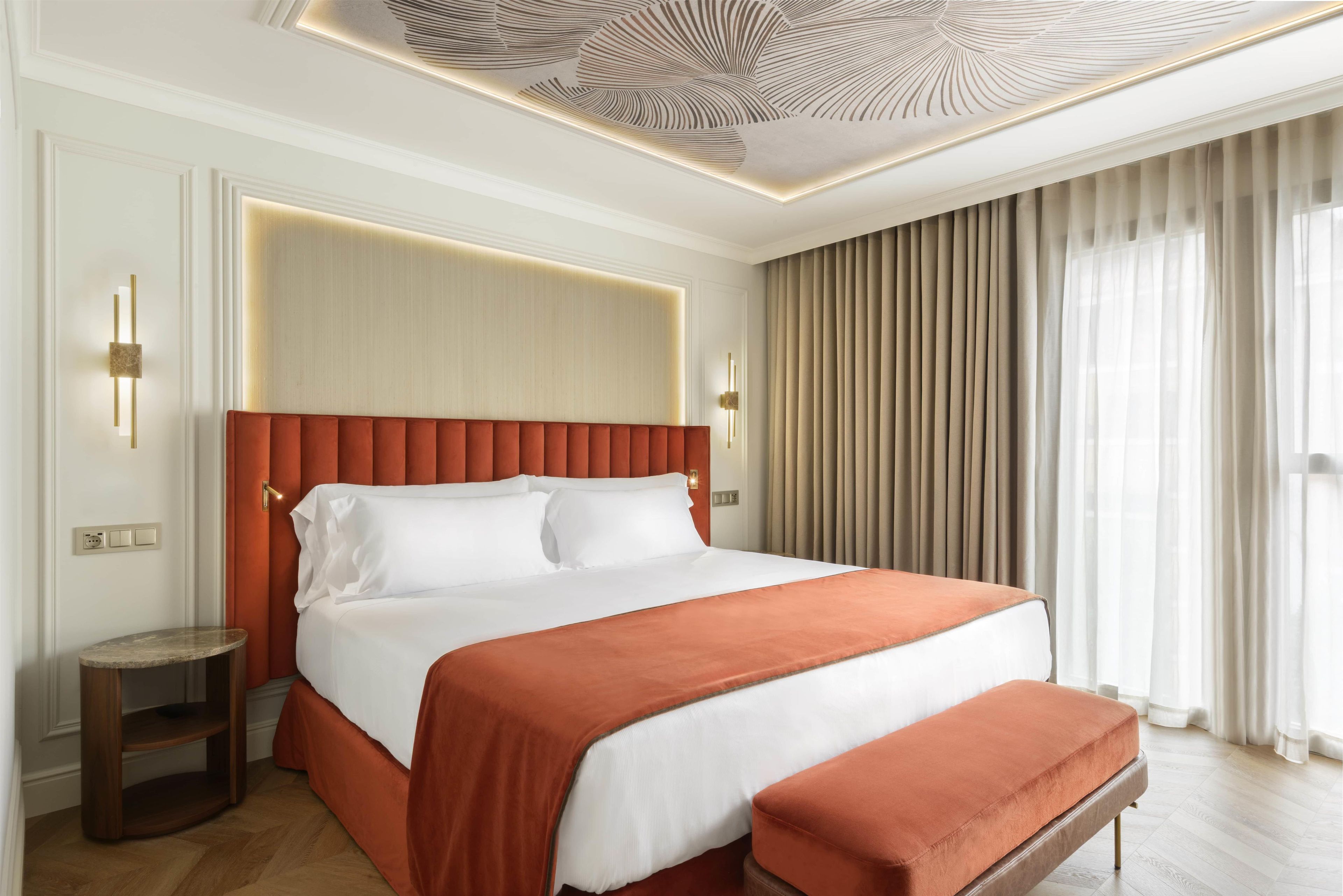 A hotel room with a large bed, a bench, a nightstand, and a ceiling with a decorative pattern.
