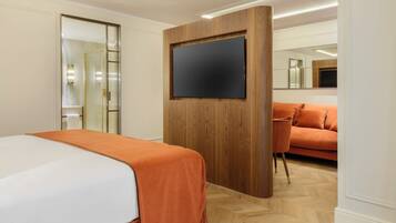 Habitación de hotel con cama, pared de paneles de madera, televisor de pantalla plana, sofá y espejo.