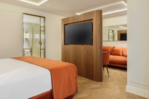 Habitación de hotel con cama, pared de paneles de madera, televisor de pantalla plana, sofá y espejo.
