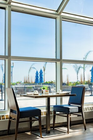 A sunlit room with large windows, a table with chairs, and a view of outdoor umbrellas and palm trees. - Ocean Place Resort And Spa (Long Branch)