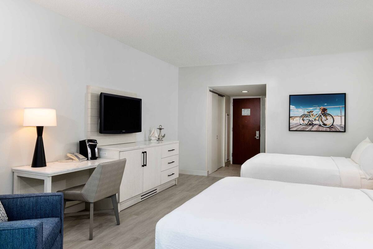 A hotel room with a bed, a desk with a chair, a television, and a painting on the wall.