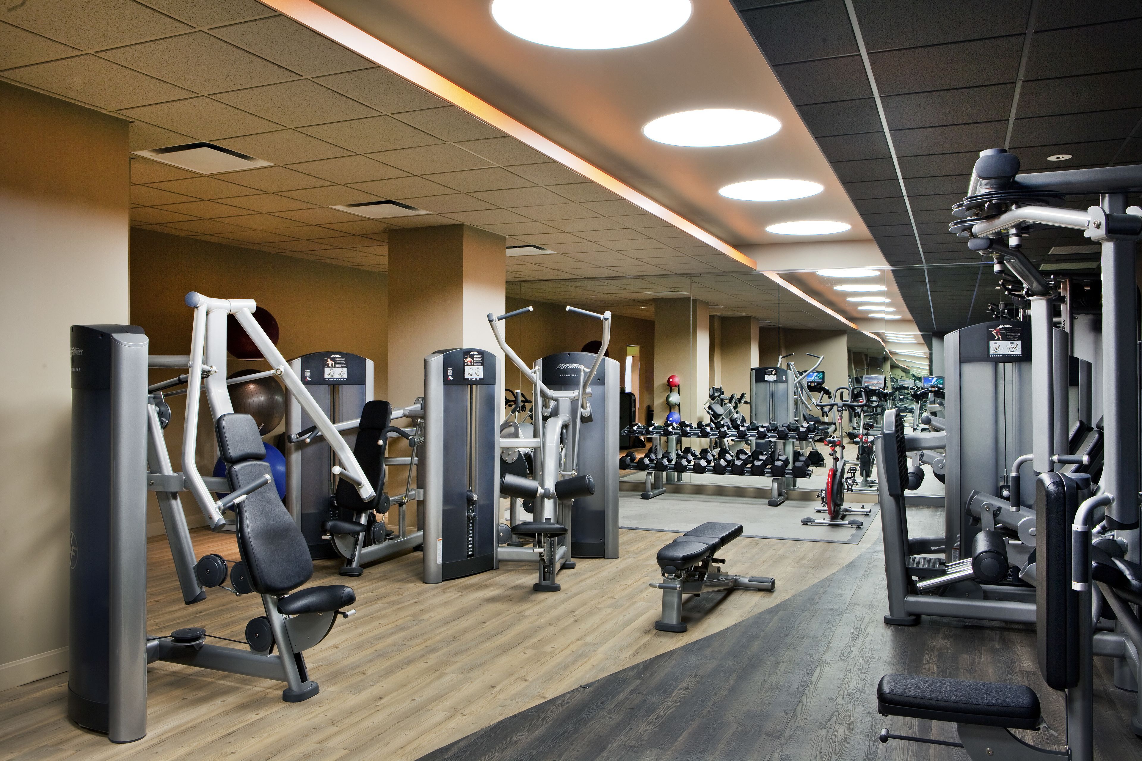 A gym with various exercise machines, benches, and a wooden floor.