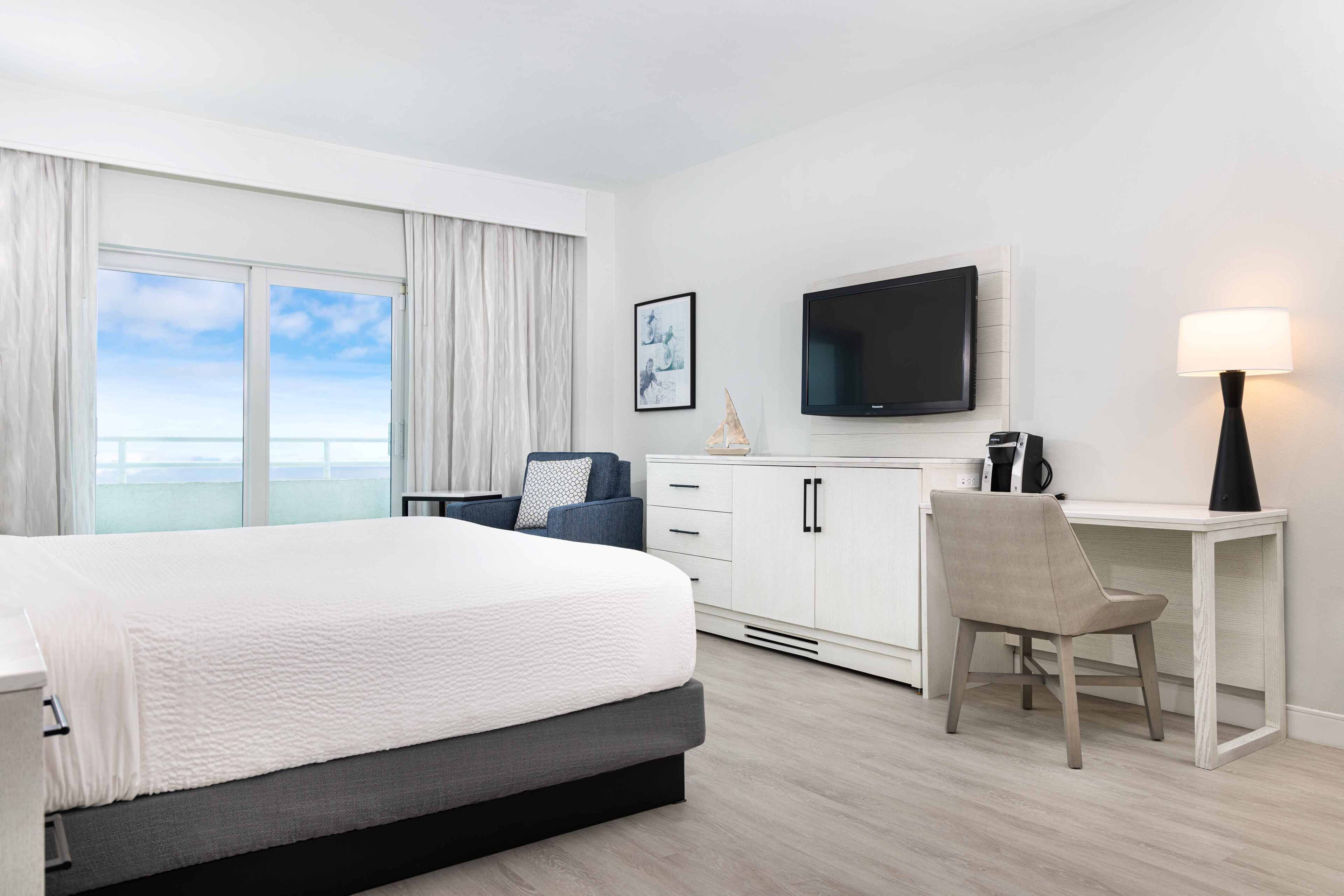 Habitación de hotel con cama, escritorio, silla, televisor y vista al mar.